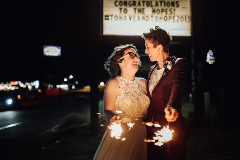 Same sex couple holding sparklers under their wedding sign