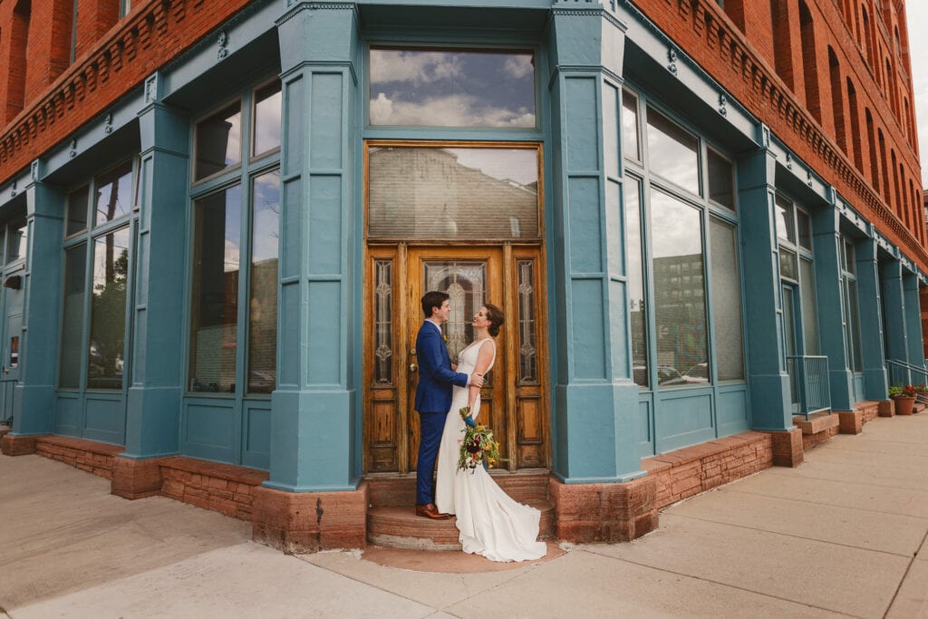 Couple in wedding attire symmetrically framed on the corner of a turquoise building in Denver.