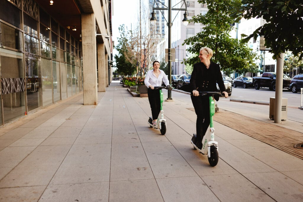 Couple riding Lime scooters down a city sidewalk after eloping in Denver, Colorado.